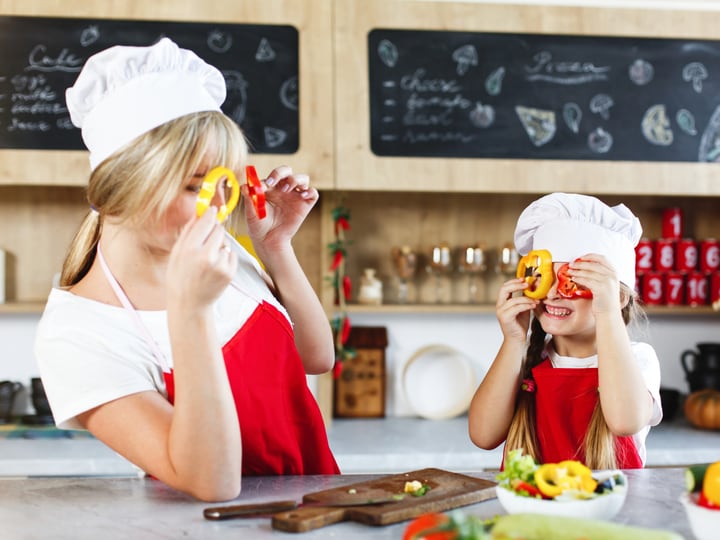 Two young children in chef hats baking together, an adult helping